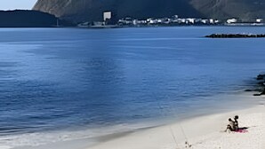 Uma praia com vista clara para uma montanha ao fundo, água calma e faixa de areia.