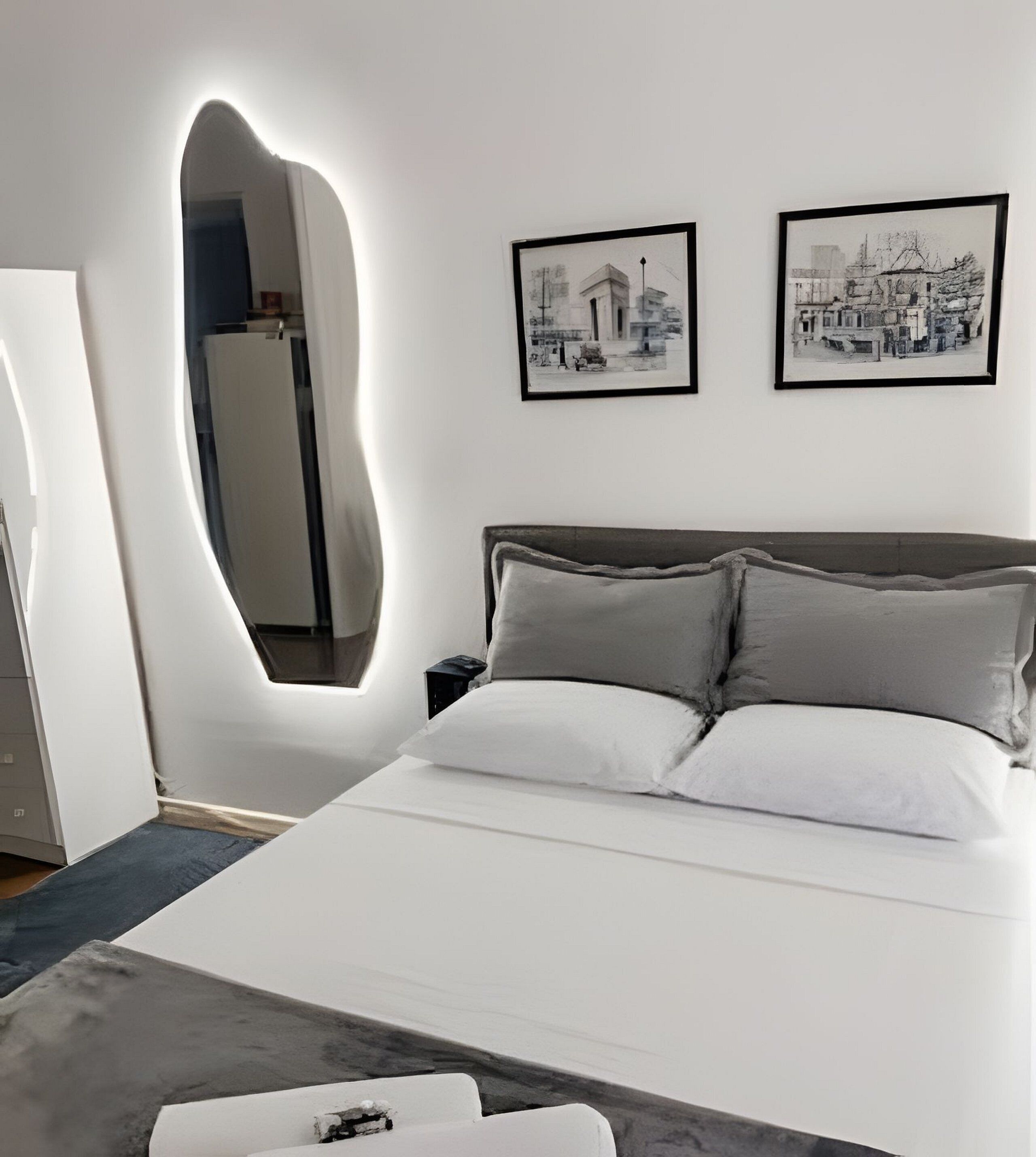 Une chambre moderne avec un grand lit, un miroir et deux tableaux encadrés accrochés au mur.