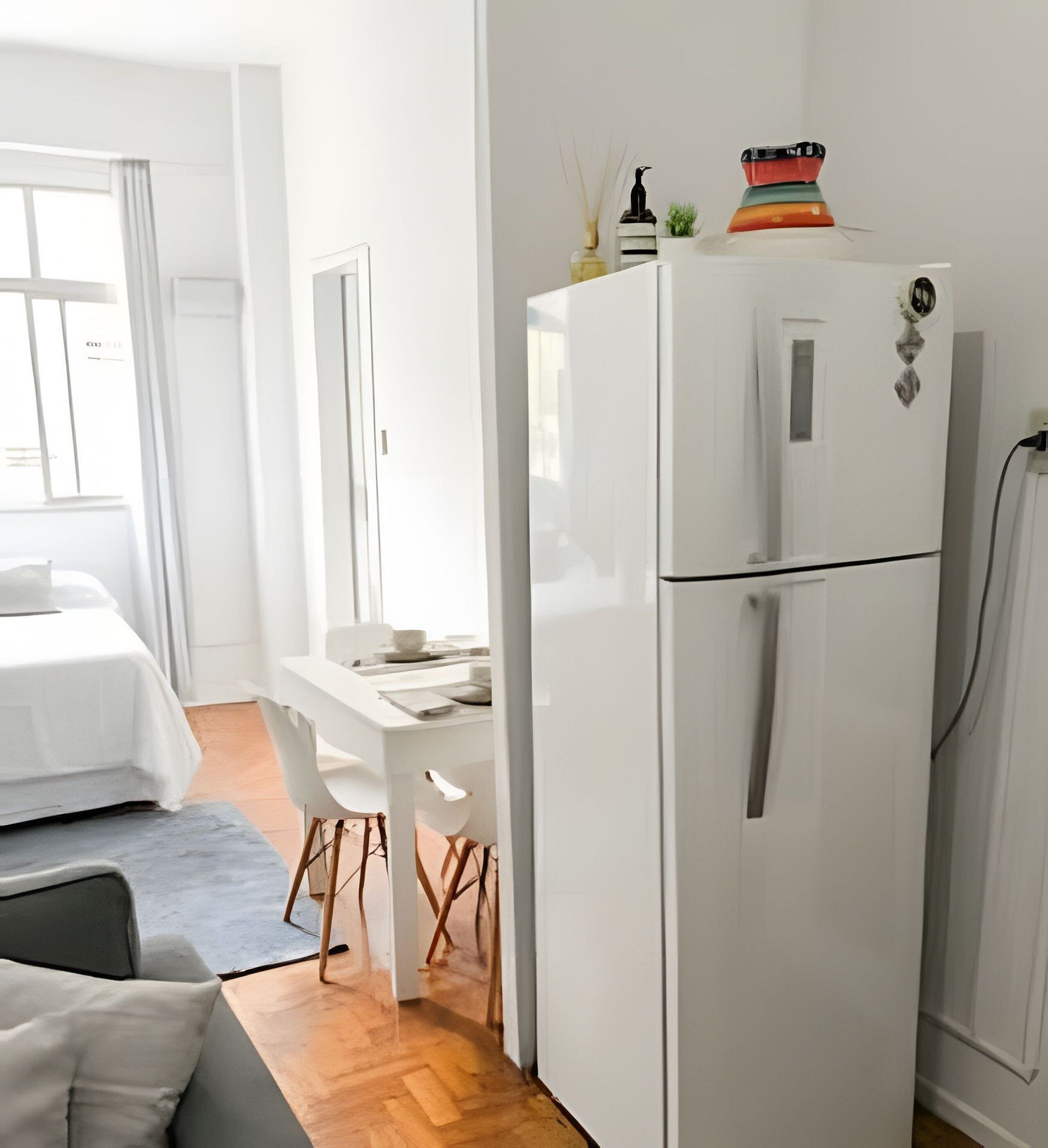 Una cocina moderna y minimalista con un refrigerador blanco, una mesa de comedor con sillas y un ventanal que proporciona luz natural.