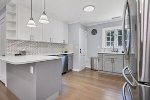 Una cocina moderna con una isla central, iluminación colgante y un refrigerador de acero inoxidable.