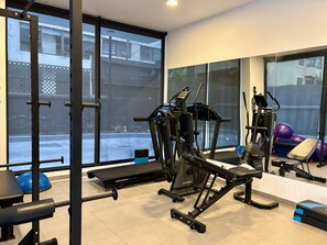 Ein Fitnessraum mit Trainingsgeräten, großen Fenstern und Blick ins Freie.