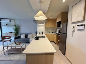 A modern kitchen with a central island, wooden cabinets, a built-in microwave, and a refrigerator.