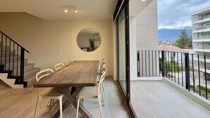 Ein Essbereich mit Holztisch und -stühlen, einem runden Spiegel an der Wand und einem Balkon mit Blick auf Gebäude und Berge.