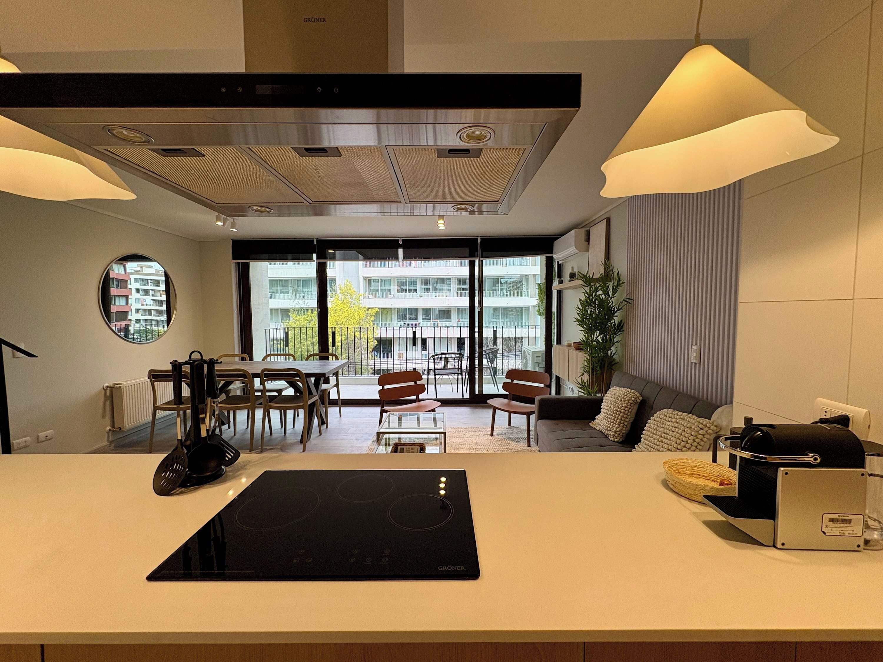 A modern kitchen with a built-in stove, dining area with chairs, a sofa, and a view of the outside balcony.