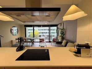 A modern kitchen with a built-in stove, dining area with chairs, a sofa, and a view of the outside balcony.