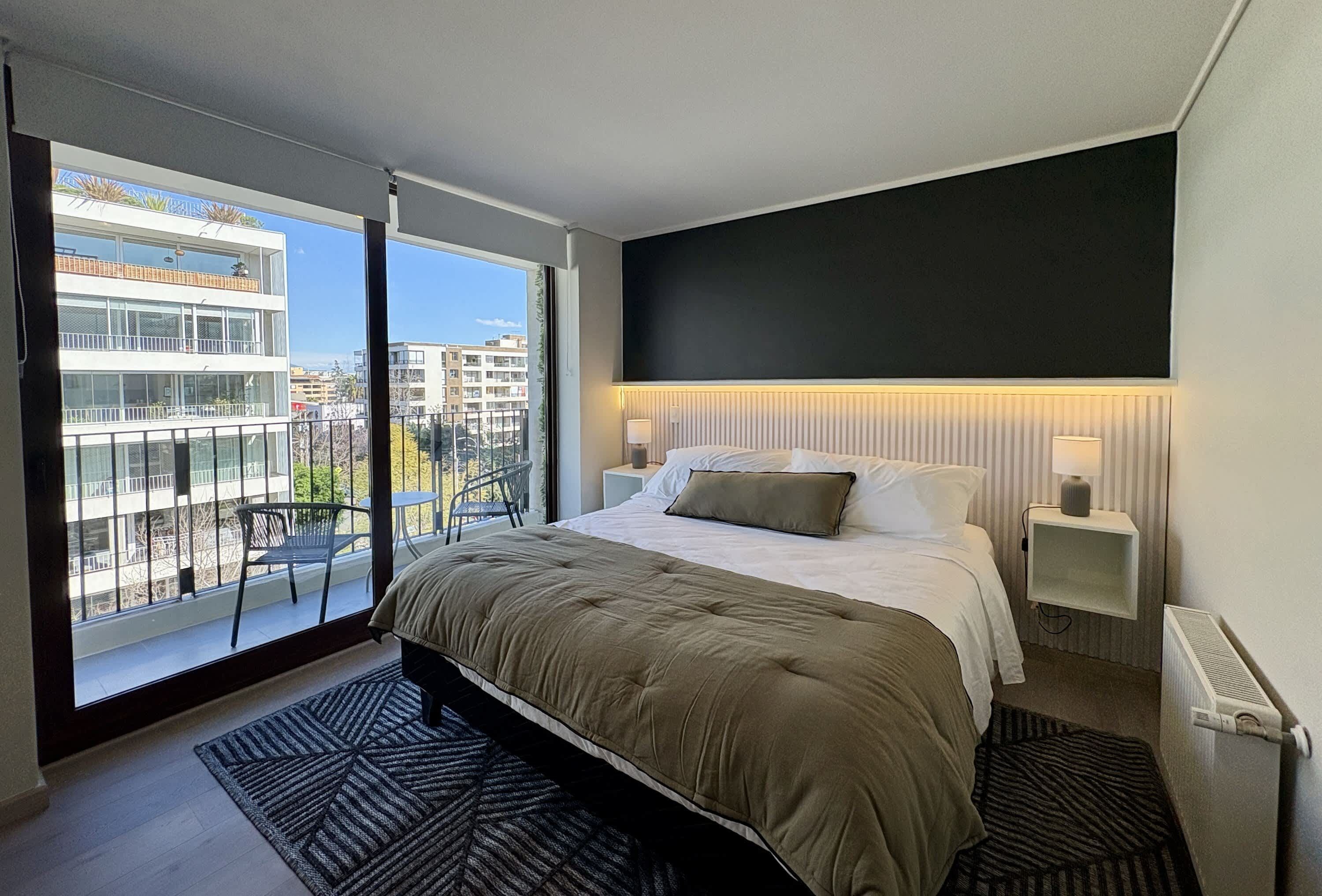 A modern bedroom with a large bed, a view of the city through a sliding door, and a black accent wall.