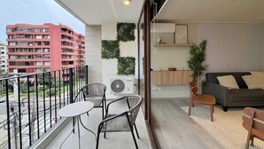 Ein Balkon mit Tisch und Stühlen, Blick auf ein rotes Gebäude sowie ein Wohnbereich mit einer Couch und Kissen.