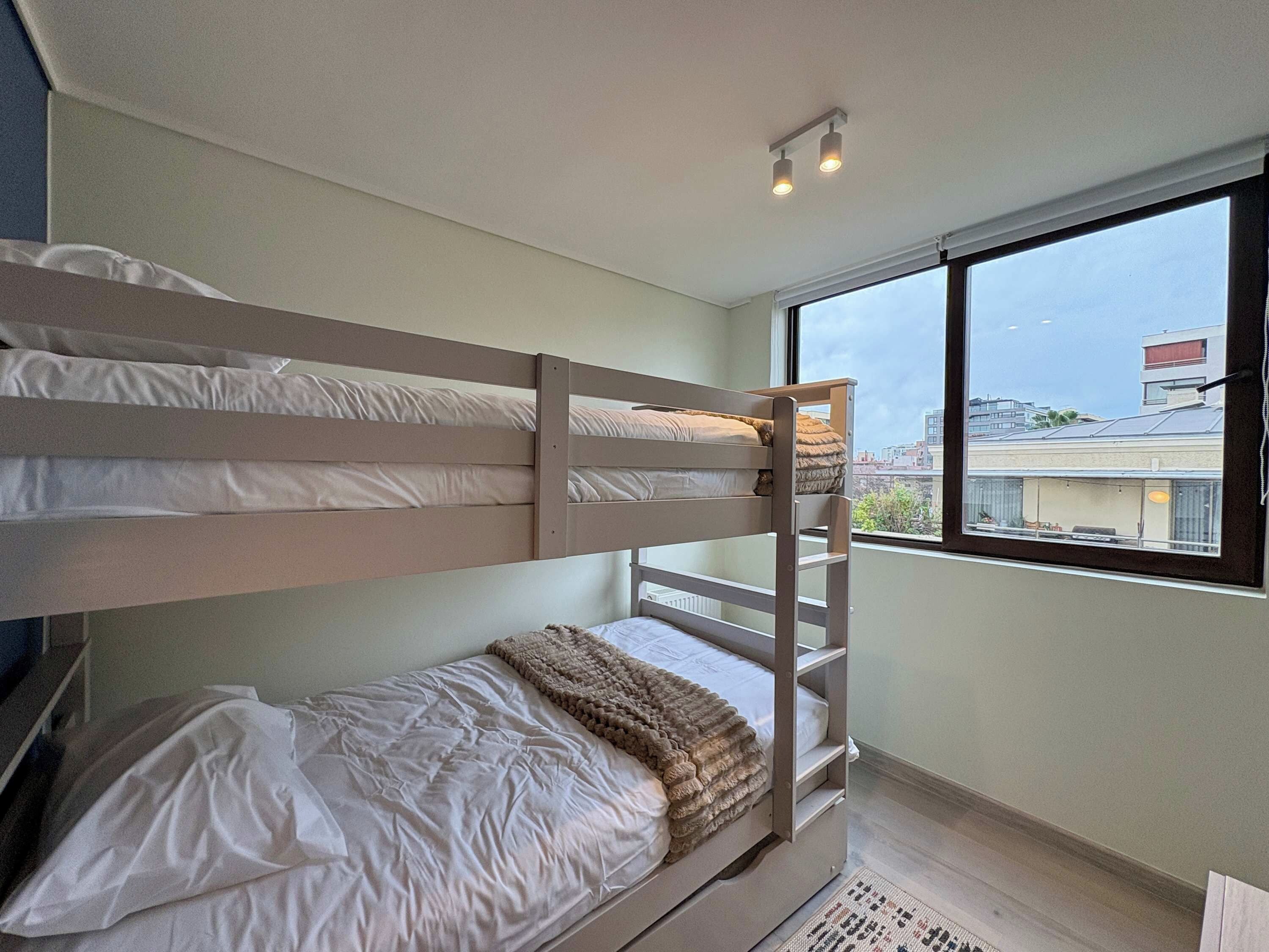 A bunk bed room with a window, a radiator, and a small rug.