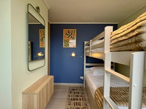 Ein kleines Zimmer mit Etagenbetten, einem Spiegel, einer Wandlampe und einem gemusterten Teppich.