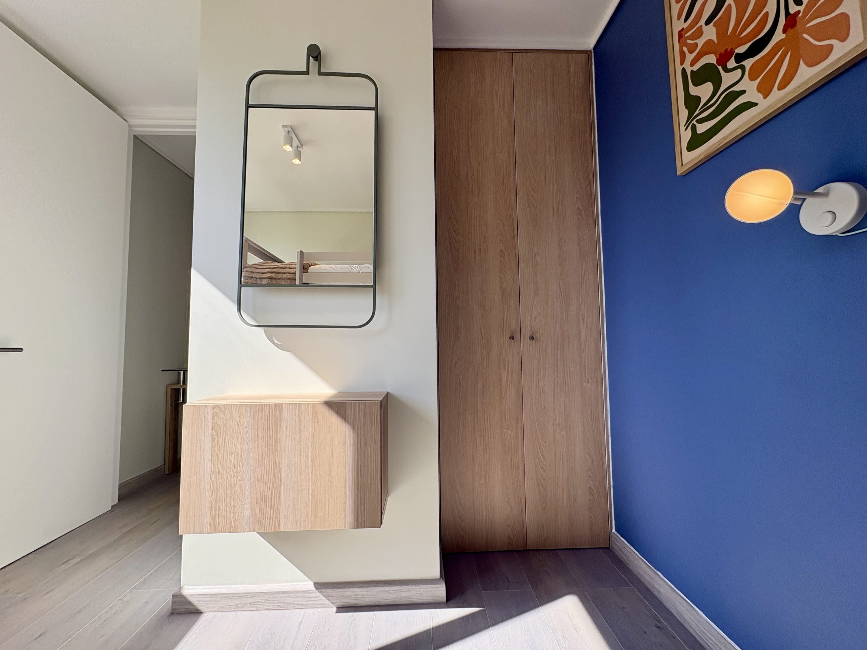 A bathroom with a wooden vanity, a mirror, and a wall-mounted light fixture.