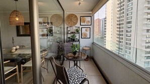 A balcony with a dining area, wicker chairs, a round table, and a view of a high-rise building.