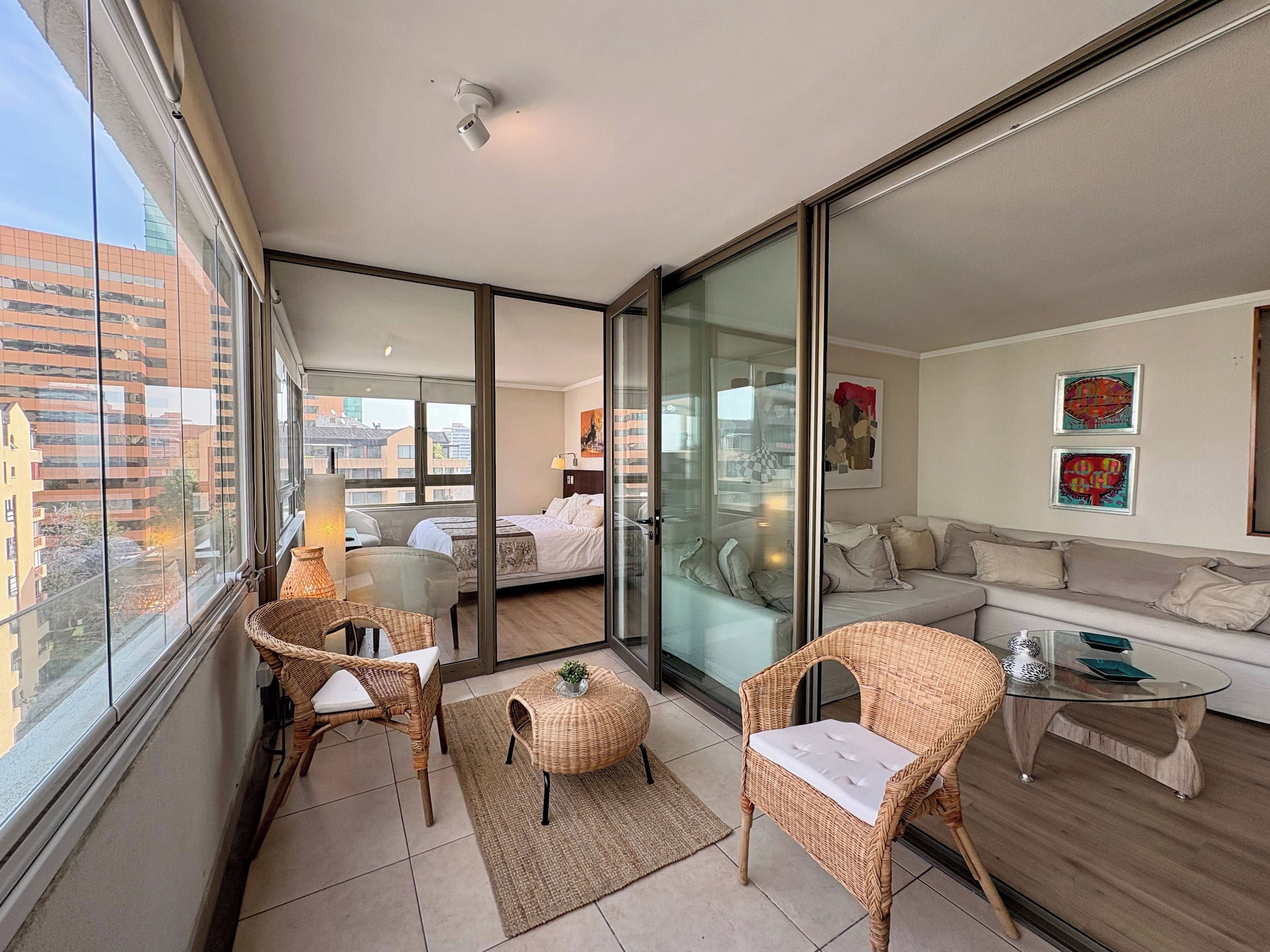 Un appartement moderne doté d’un balcon, d’un ensemble de canapés, de meubles en osier et d’œuvres d’art accrochées aux murs.