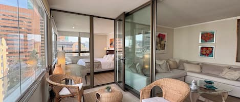 A modern apartment with a balcony, a sofa set, wicker furniture, and artwork on the walls.