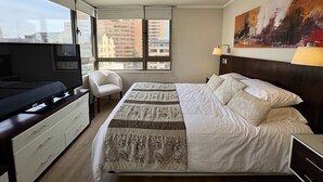 A hotel room with a bed, a desk, a chair, a TV, and a large window with a city view.