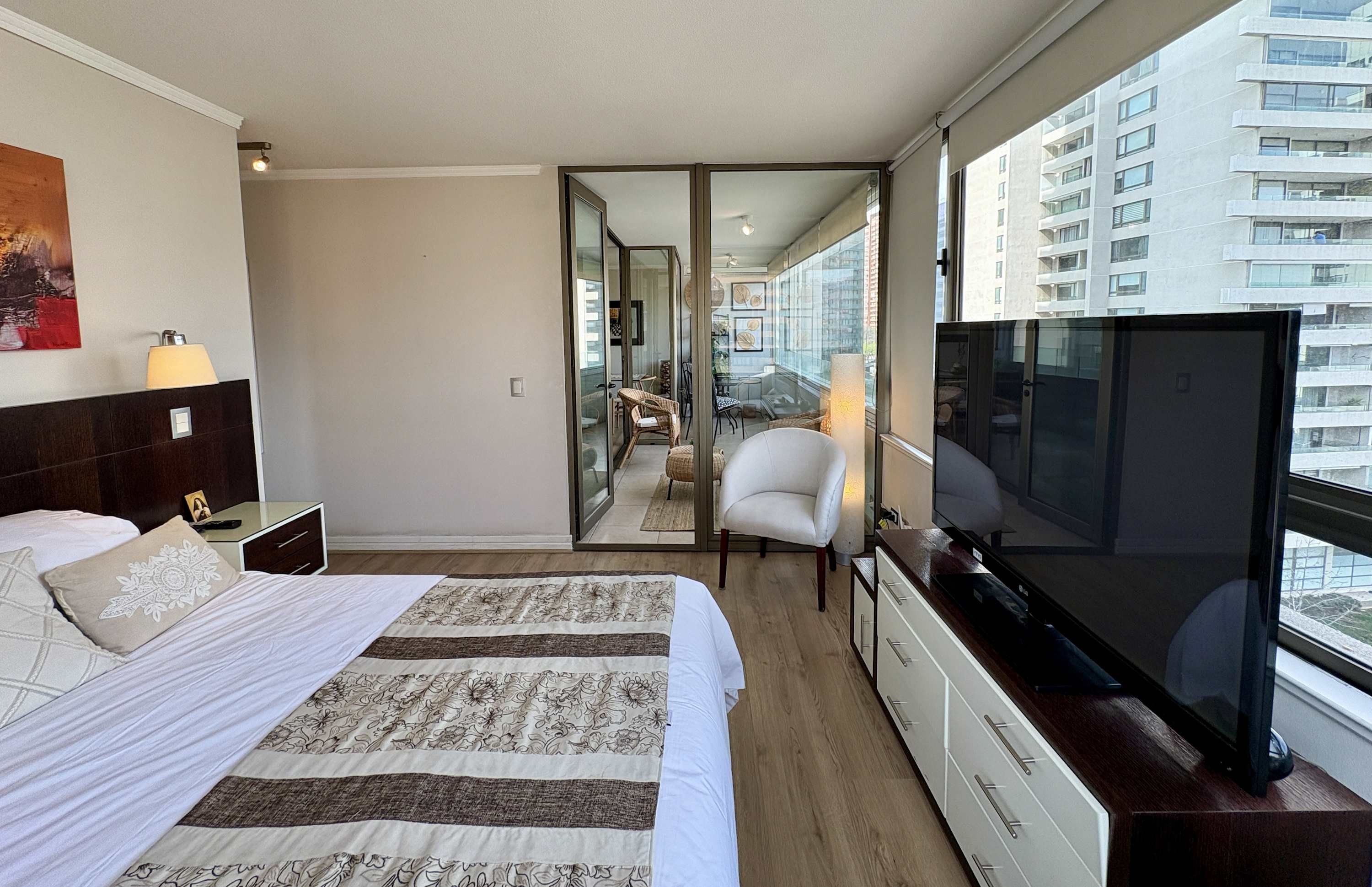 A hotel room with a large bed, a TV, a desk, and a view of the city through the window.