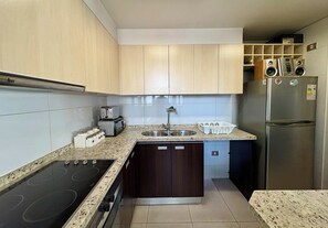 A compact kitchen with a built-in oven, a sink, and a refrigerator. - 2BR Las Condes - Parking, Indoor Pool & Laundry (Las Condes)