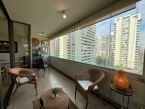 A balcony with wicker furniture, a table, and a potted plant. - 2BR Las Condes - Parking, Indoor Pool & Laundry (Las Condes)