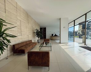 A modern lobby with a sofa, armchairs, a coffee table, and a reception desk. - 2BR Las Condes - Parking, Indoor Pool & Laundry (Las Condes)