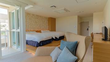 A hotel room with two beds, a sofa, a TV, and a sliding glass door to the outside.