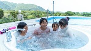Un jacuzzi con cuatro personas, rodeado por una piscina y vegetación.