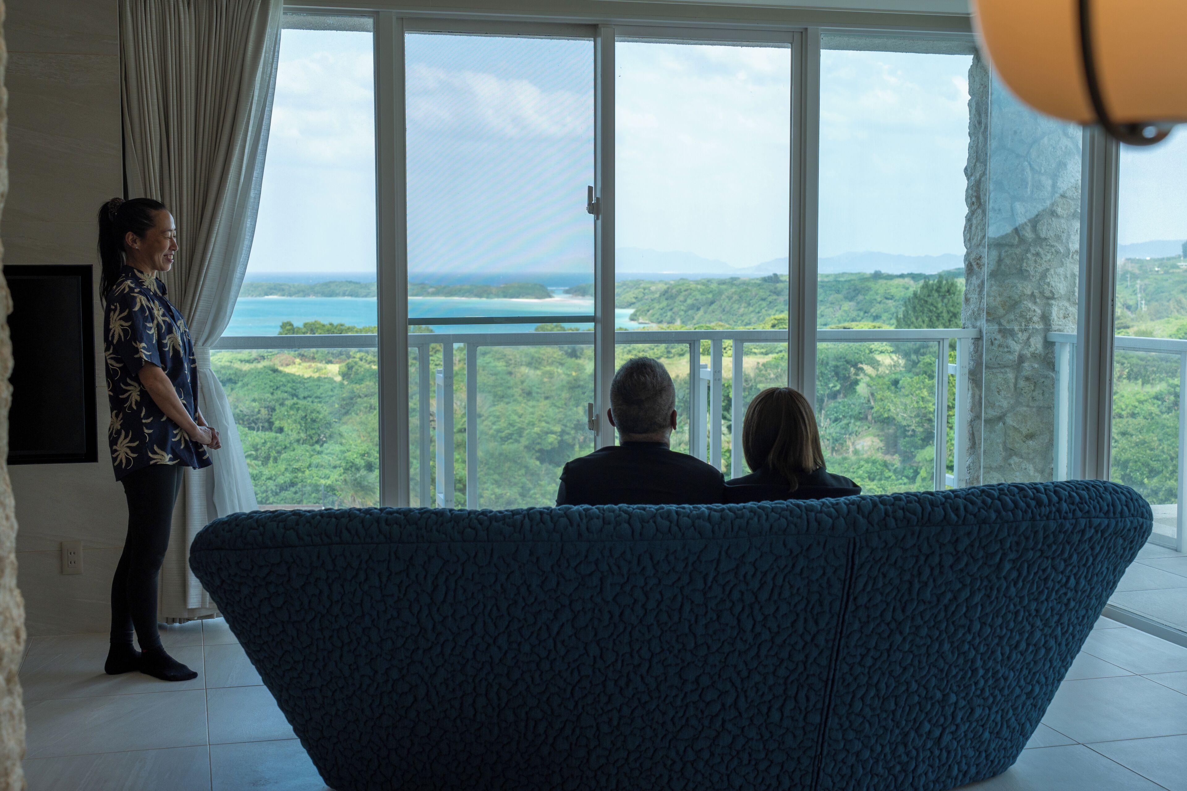 A room with a large window, a blue sofa, and a person standing by the window.