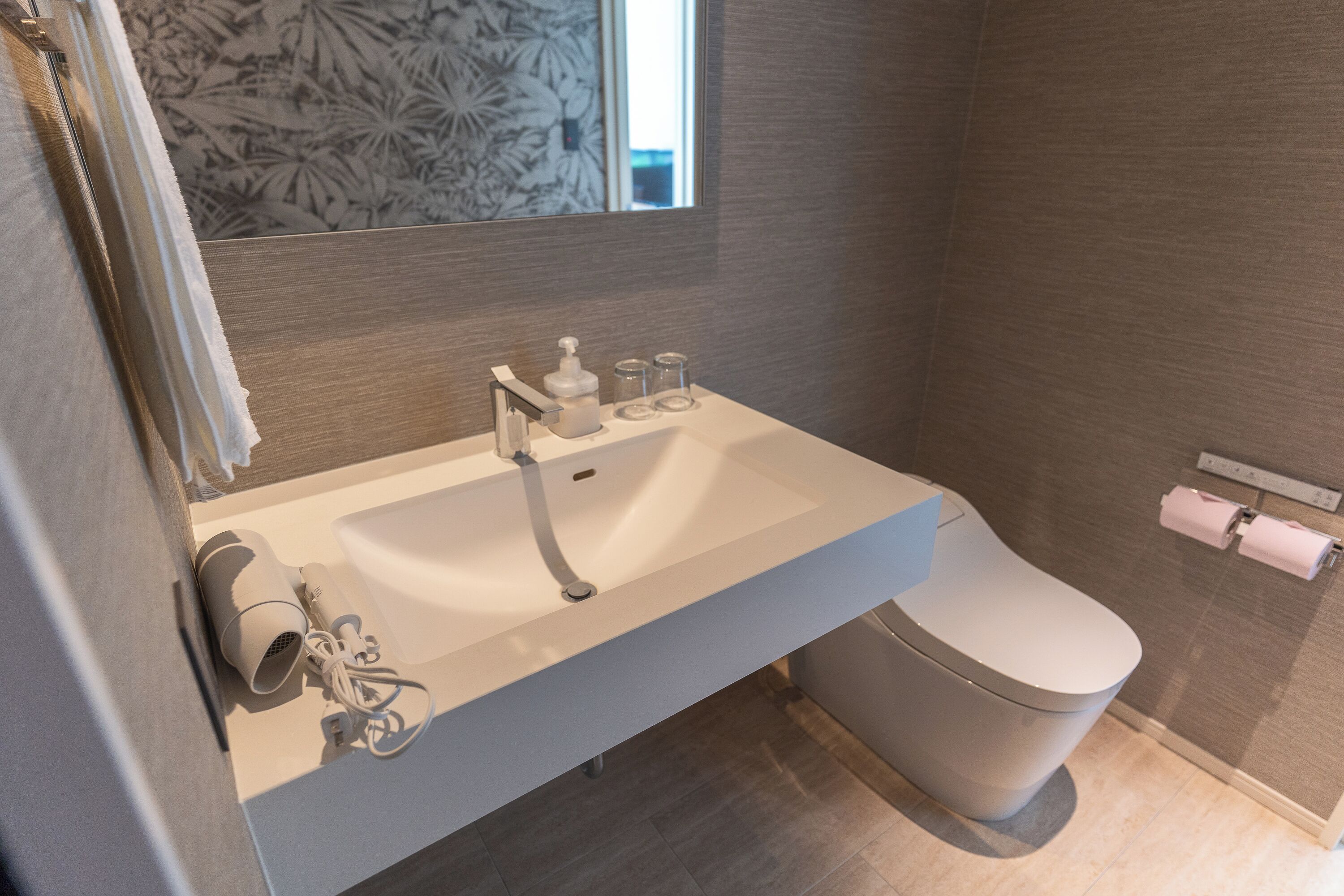 Een moderne badkamer met een wastafel, toilet en zeepdispenser.