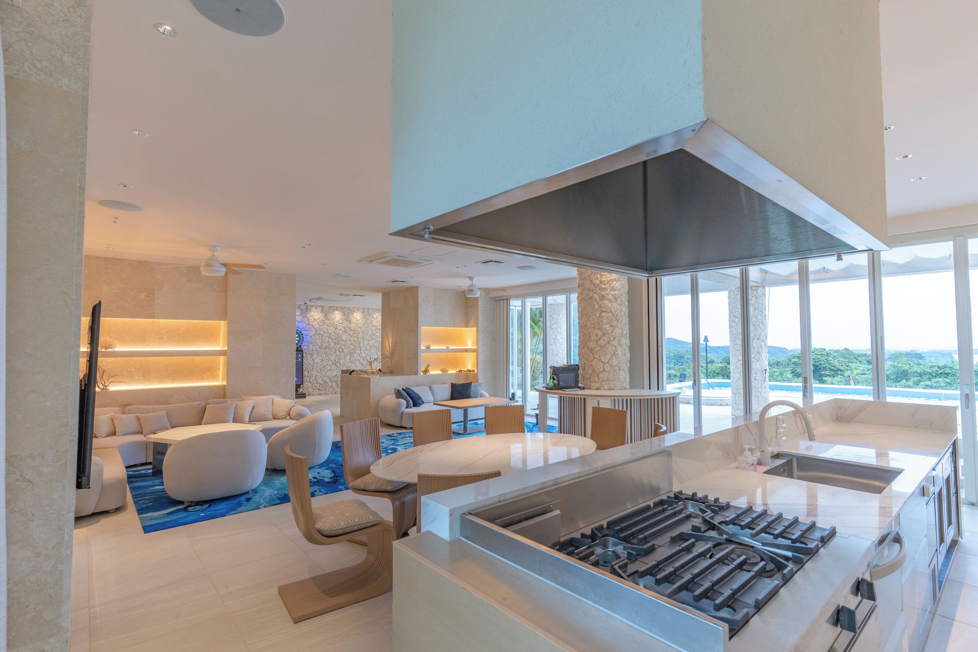 Una cocina moderna con una isla grande, un comedor con mesa redonda y un área de estar con sofás y sillas.