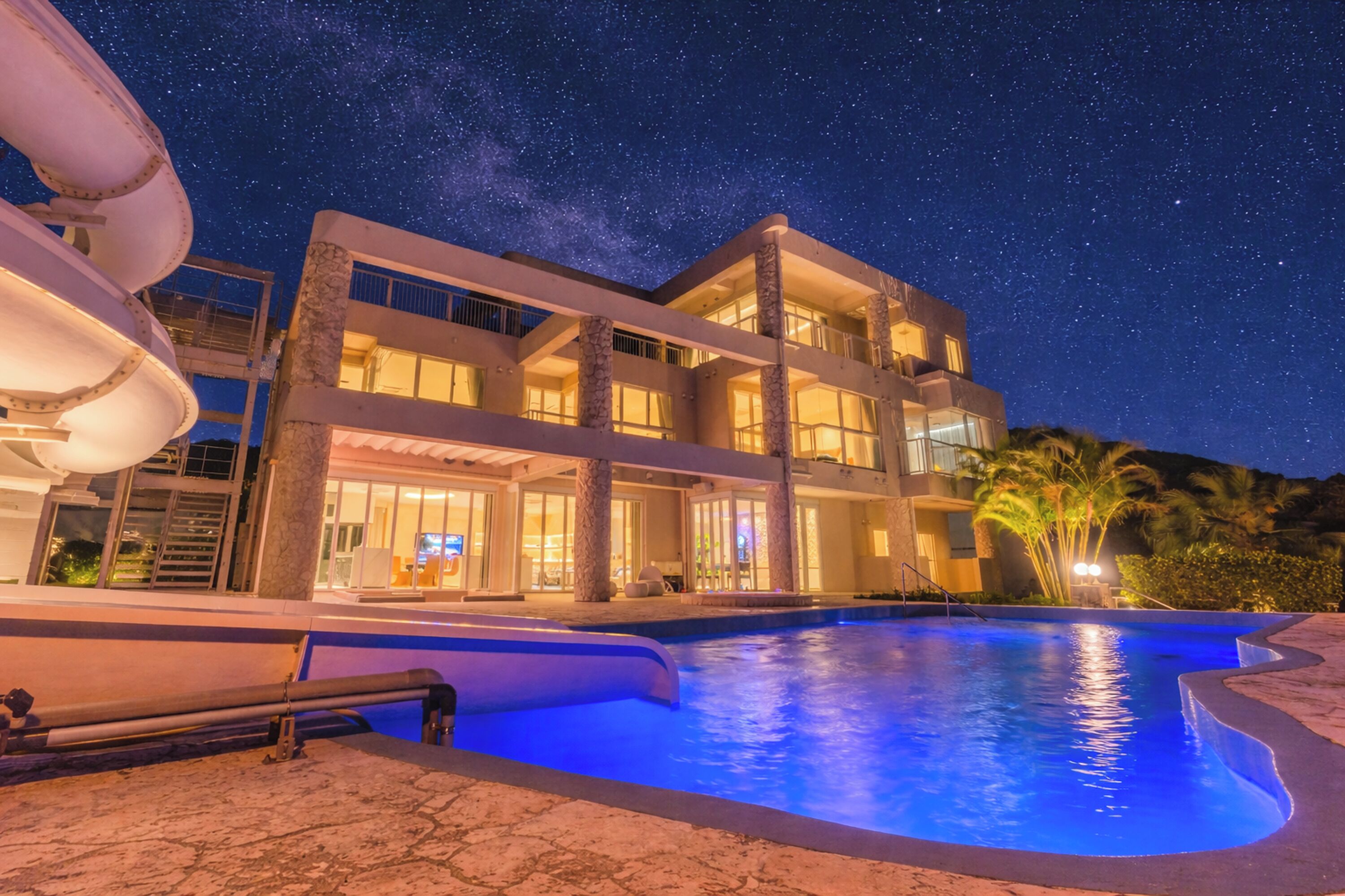 A modern hotel with a swimming pool, multiple floors, and a starry night sky.