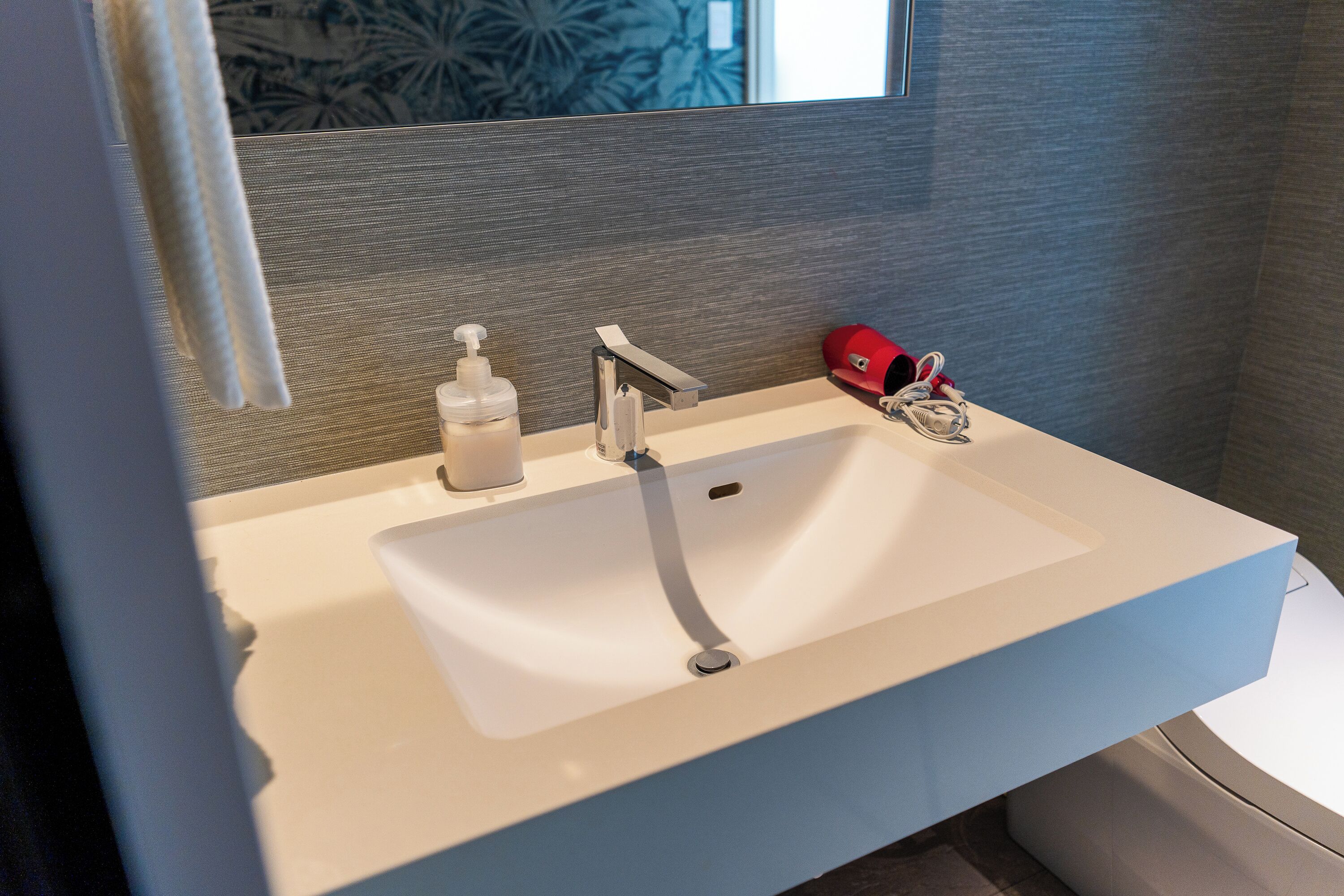 A bathroom with a white sink, a soap dispenser, a faucet, and a red object on the counter.