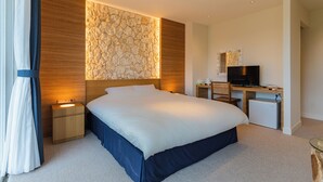 Una habitación de hotel moderna con una cama grande, un escritorio con televisor, un refrigerador pequeño y una pared de acento de piedra.