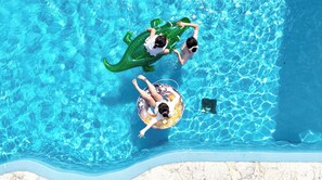 An aerial view of a swimming pool with clear blue water, two people floating on inflatable rings, and a stone-lined pool edge. - SEARTH KABIRA (Ishigaki)