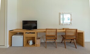 A room with a wooden desk, two wicker chairs, a television, a small refrigerator, and a decorative mirror. - SEARTH KABIRA (Ishigaki)