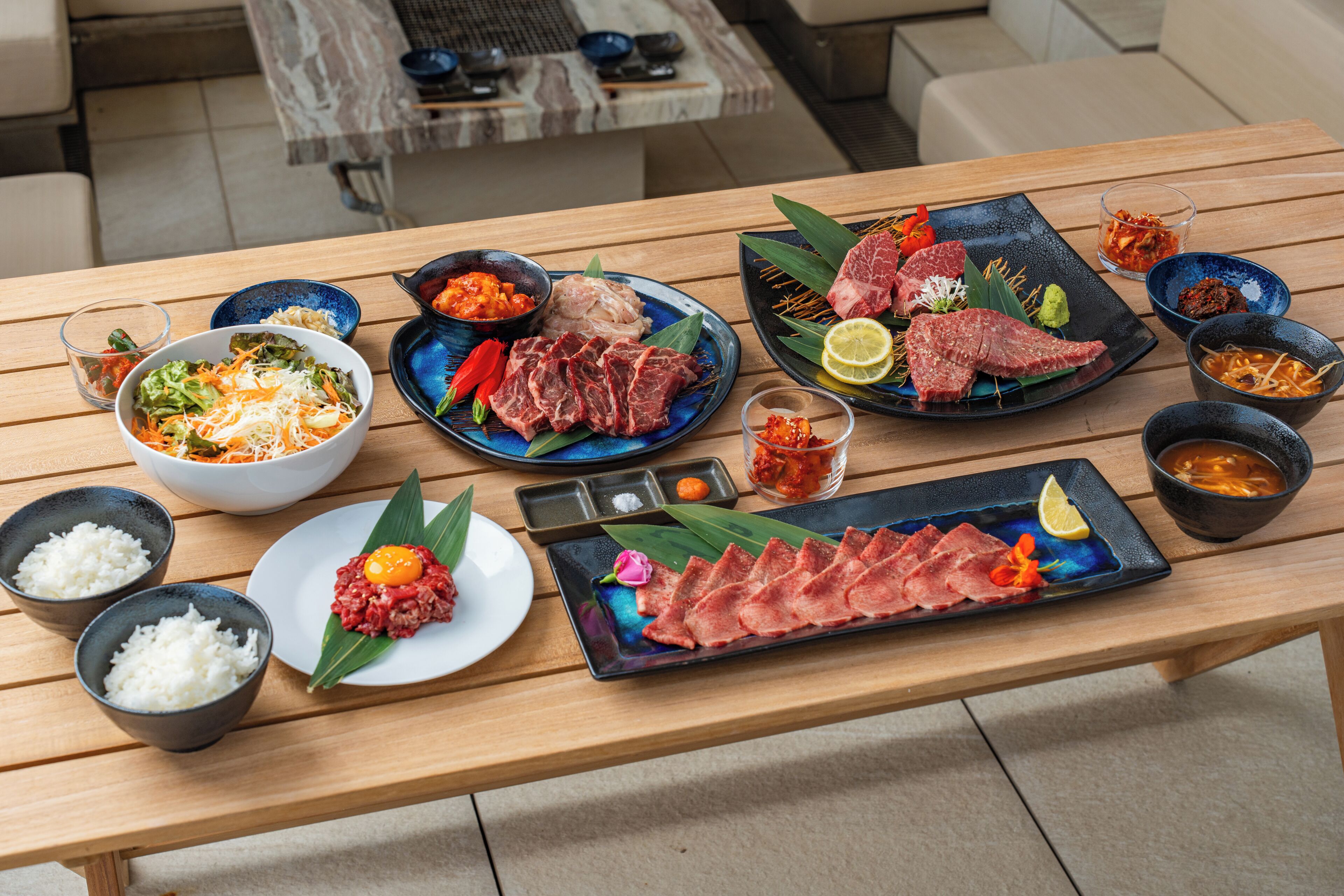A wooden table with various dishes, including meat, rice, and vegetables.