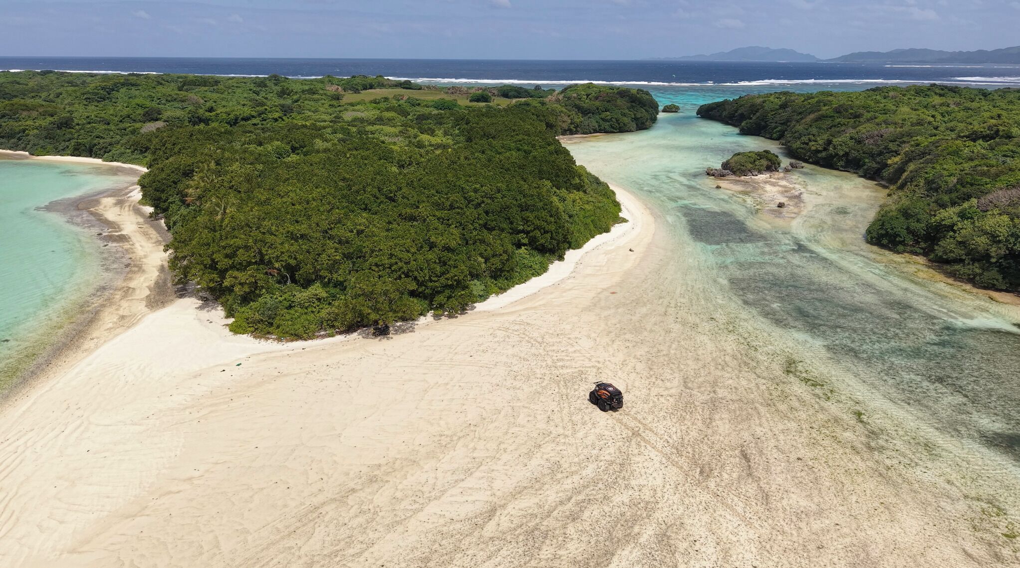 Vista aérea de una playa con aguas turquesas cristalinas, vegetación verde exuberante y una orilla arenosa.