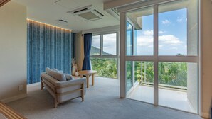 Una habitación moderna con sofá, una mesita y amplios ventanales con vistas a zonas verdes y montañas.