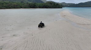 A sandy beach with a person riding a quad bike. - SEARTH KABIRA (Ishigaki)