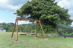 A swing set in a grassy area with a large tree in the background. - SEARTH KABIRA (Ishigaki)