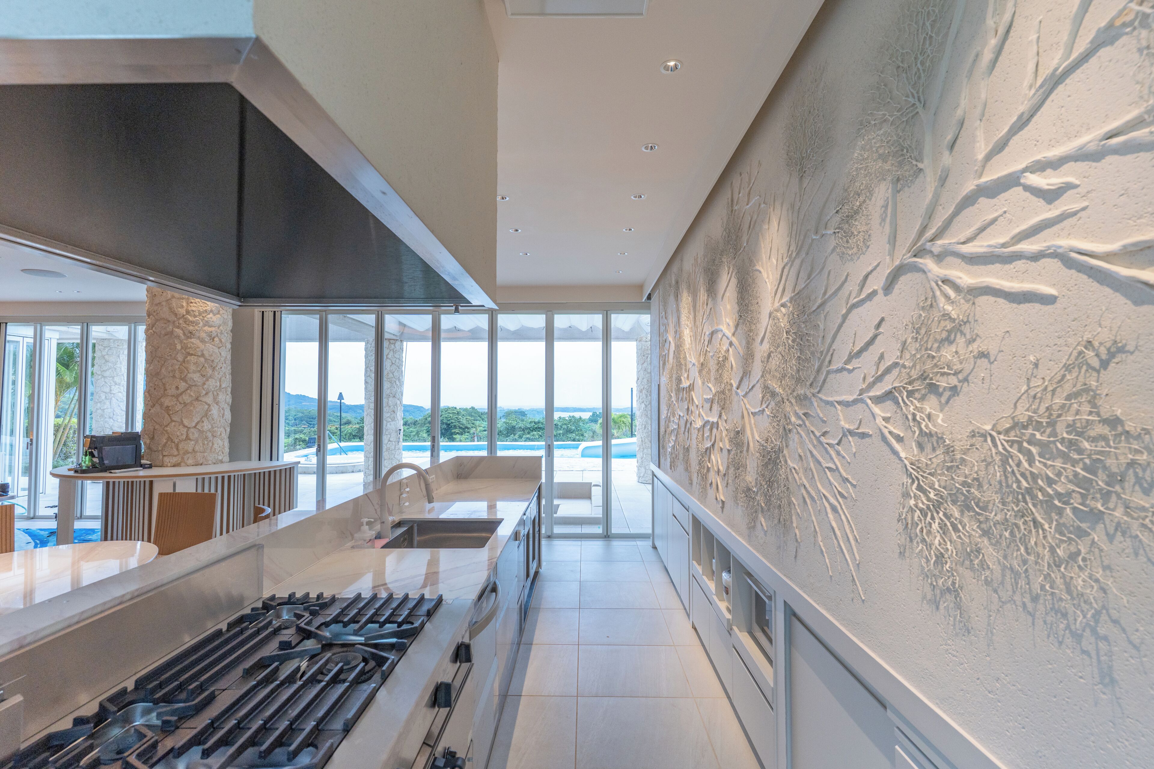 Une cuisine moderne dotée d’un grand îlot central, d’un mur d’accent en pierre et offrant une vue sur l’extérieur.