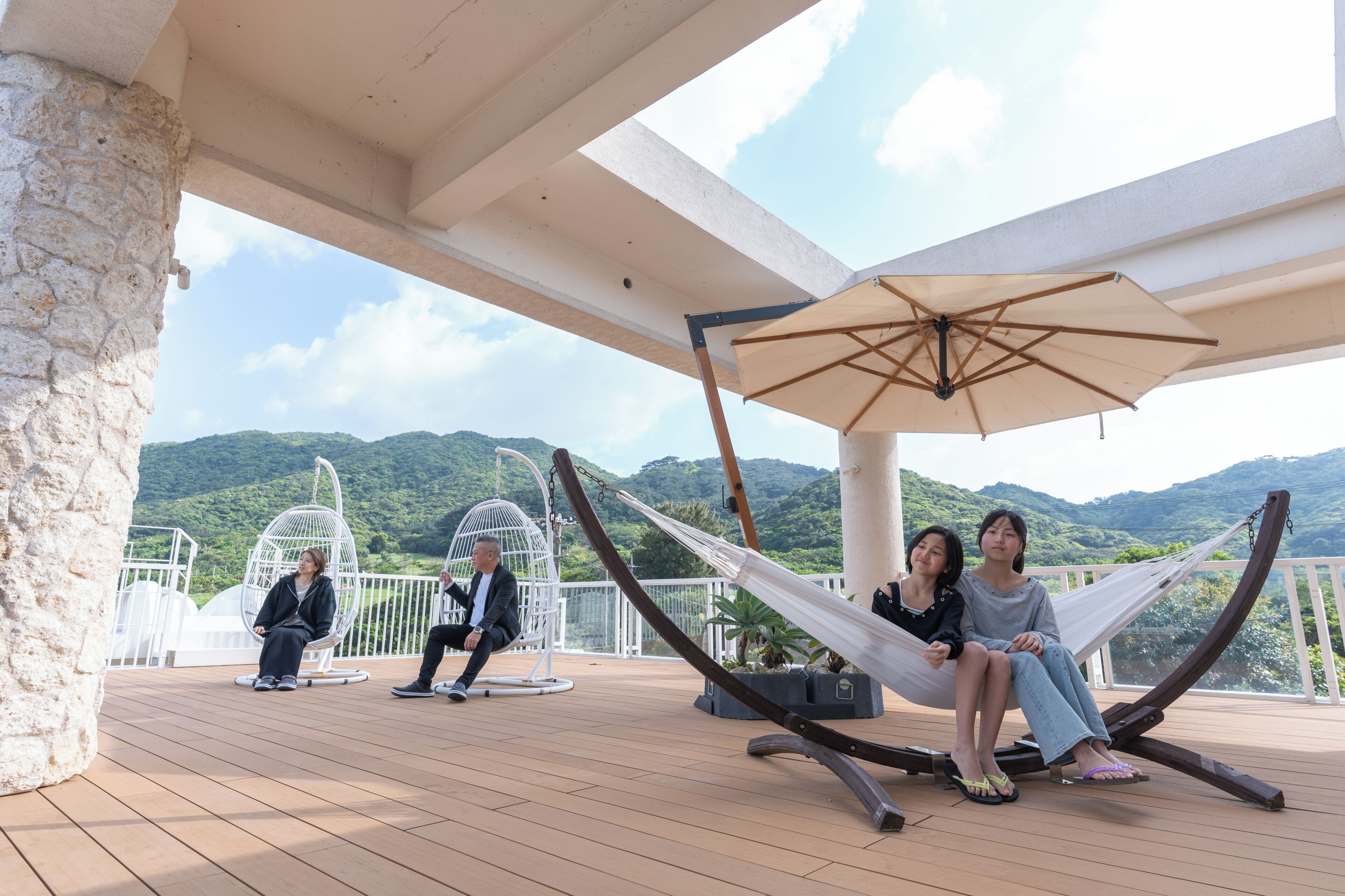 A deck with a hammock, a hanging chair, and a white umbrella.