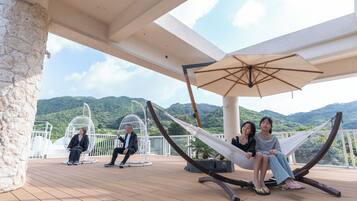A deck with a hammock, a hanging chair, and a white umbrella.