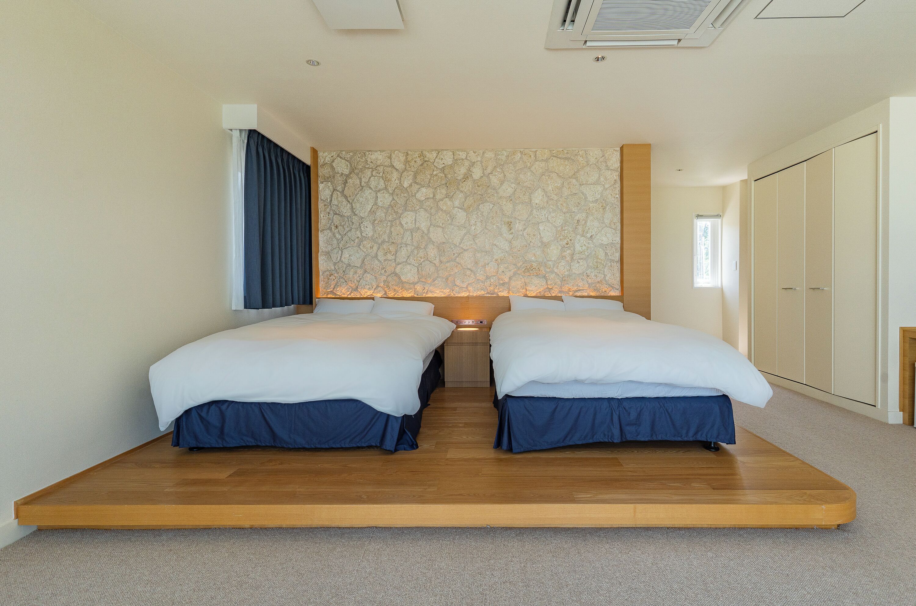 Une chambre avec deux lits, un mur en pierre, un plancher en bois et une armoire.