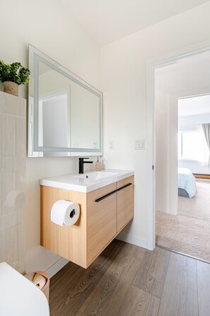 A modern bathroom with a wooden vanity, a large mirror, and a toilet paper holder. - Modern Comfort Near Seattle (Seattle)