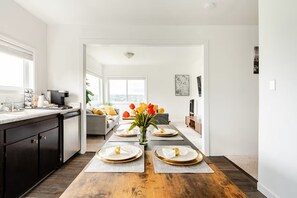 A modern kitchen with dark cabinets, a coffee machine, and a dining area with a wooden table set for four. - Modern Comfort Near Seattle (Seattle)