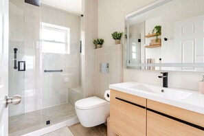 A modern bathroom with a glass shower enclosure, a toilet, a sink with a mirror, and wooden cabinets. - Modern Comfort Near Seattle (Seattle)