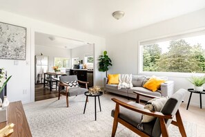 A modern living room with a grey sofa, wooden chairs, a dining area, and a kitchen in the background. - Modern Comfort Near Seattle (Seattle)