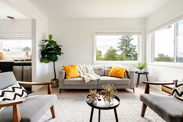 A modern living room with a grey sofa, yellow pillows, a white throw blanket, and a coffee table with decorative items. - Modern Comfort Near Seattle (Seattle)