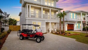 A two-story house with a garage, a red golf cart, and a well-maintained lawn. - Spiny Lobster: Private beach steps away, Heated pool & spa, Golf cart, Bunk room (Miramar Beach)