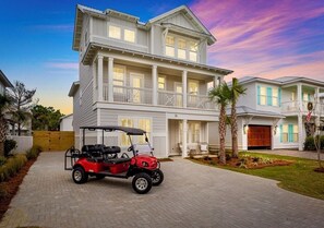 A two-story house with a garage, a red golf cart, and a well-maintained lawn. - Spiny Lobster: Private beach steps away, Heated pool & spa, Golf cart, Bunk room (Miramar Beach)