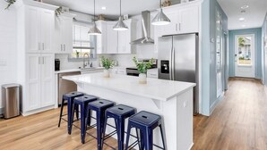 A modern kitchen with white cabinetry, stainless steel appliances, and a central island with bar stools. - Spiny Lobster: Private beach steps away, Heated pool & spa, Golf cart, Bunk room (Miramar Beach)