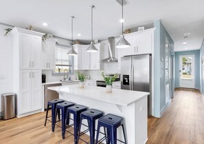 A modern kitchen with white cabinetry, stainless steel appliances, and a central island with bar stools. - Spiny Lobster: Private beach steps away, Heated pool & spa, Golf cart, Bunk room (Miramar Beach)
